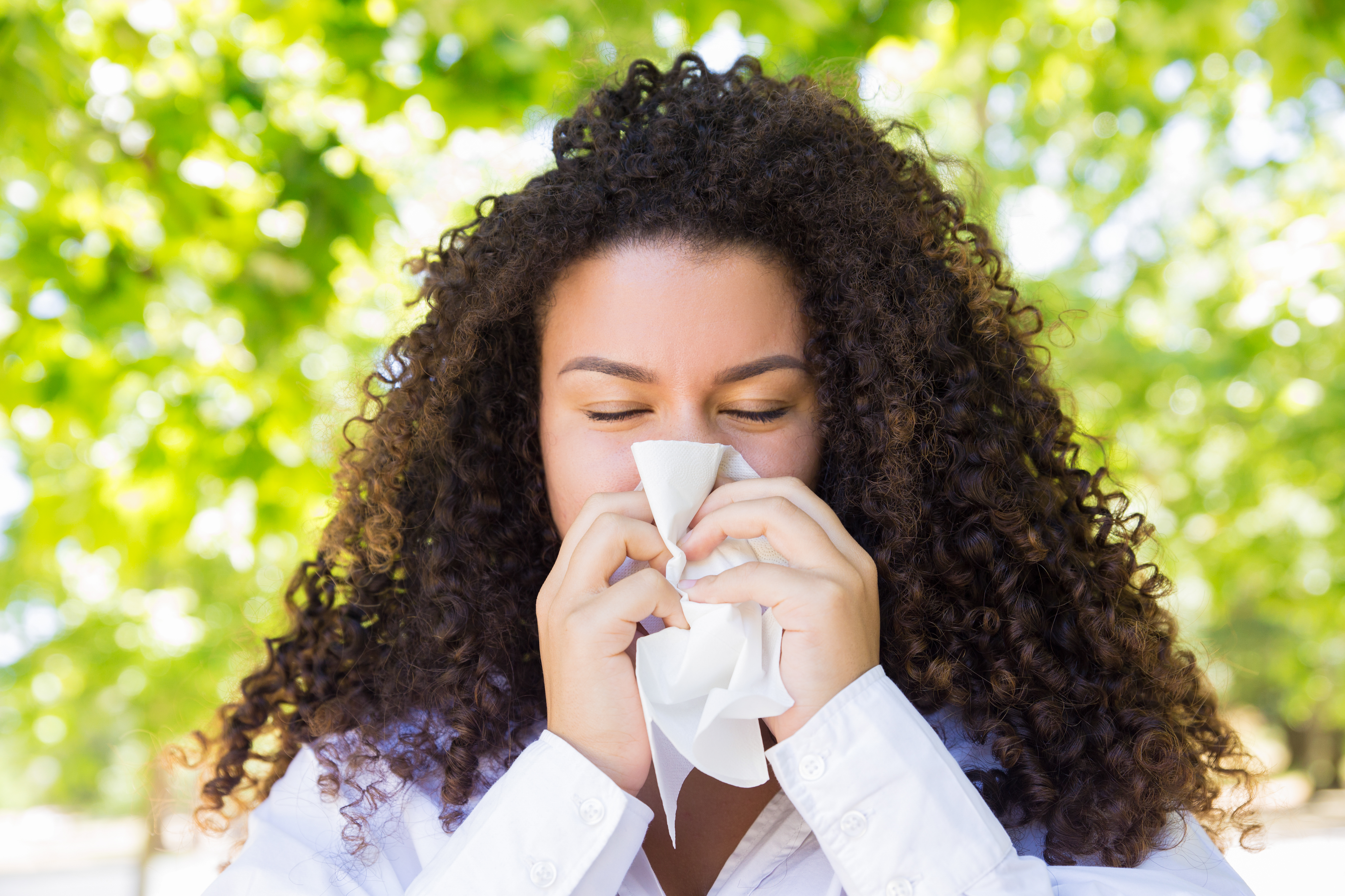 Uma mulher de cabelo cacheando assoando o nariz durante as crises alérgicas