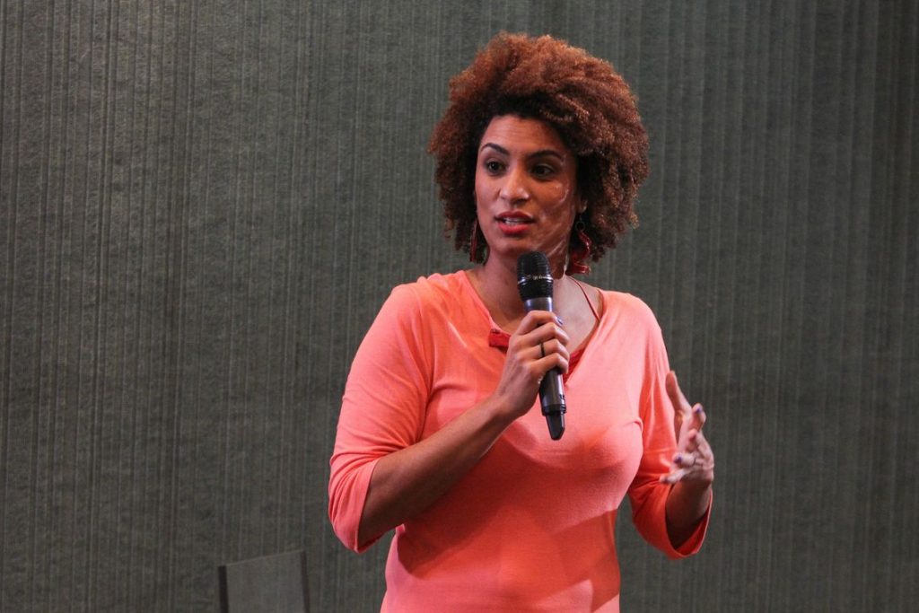 Marielle Franco com microfone discursando com uma blusa rosa