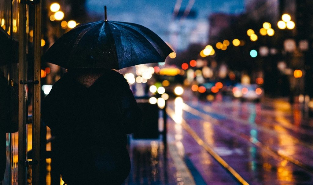 Uma mulher no ponto de ônibus com uma sombrinha para se proteger da chuva. Foto: Pixabay