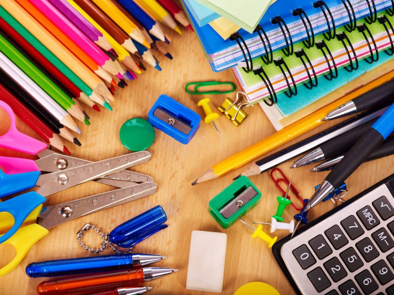 Lápis de cor, apontador, calculadora, canetas e outros tantos materiais escolares em cima de uma mesa de madeira.