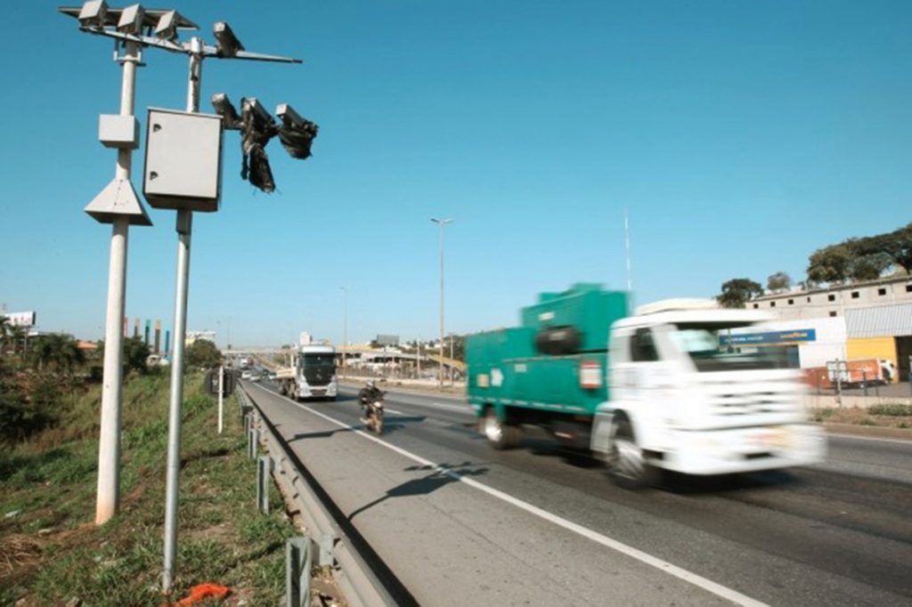 Radares de fiscalização instalado ao lado da rodovia. É possível ver caminhões e uma moto na estrada
