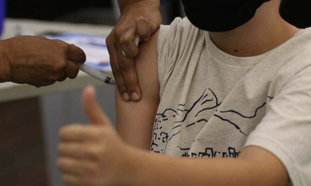Duas mãos no braço de uma criança que está recebendo uma vacina