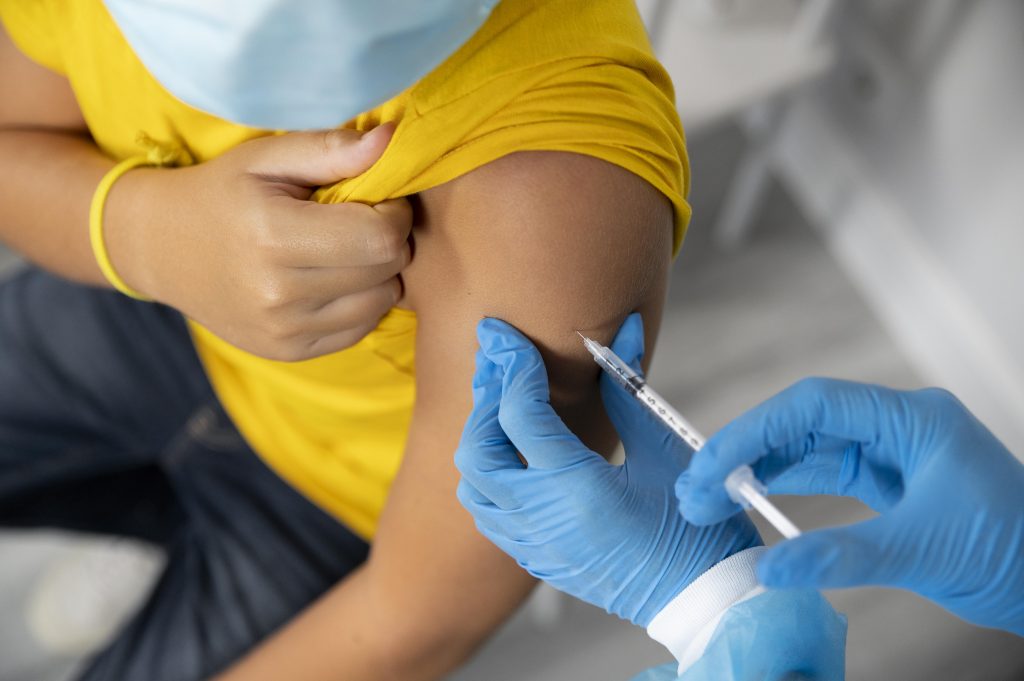 Vacina da dengue sendo aplicada em um adolescente de camisa amarela
