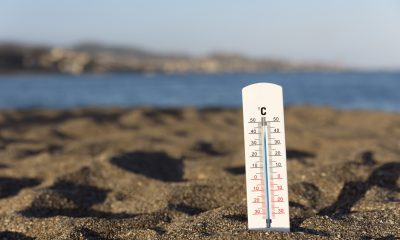 Termômetro afundado na areia com o mar ao fundo.