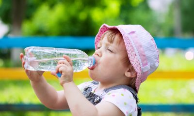 Uma menininha de chapéu rosa bebendo água na garrafa. Foto: FreePik