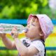 Uma menininha de chapéu rosa bebendo água na garrafa. Foto: FreePik