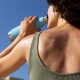 Mulher de costas bebendo água no calor ao ar livre. Foto: FreePik