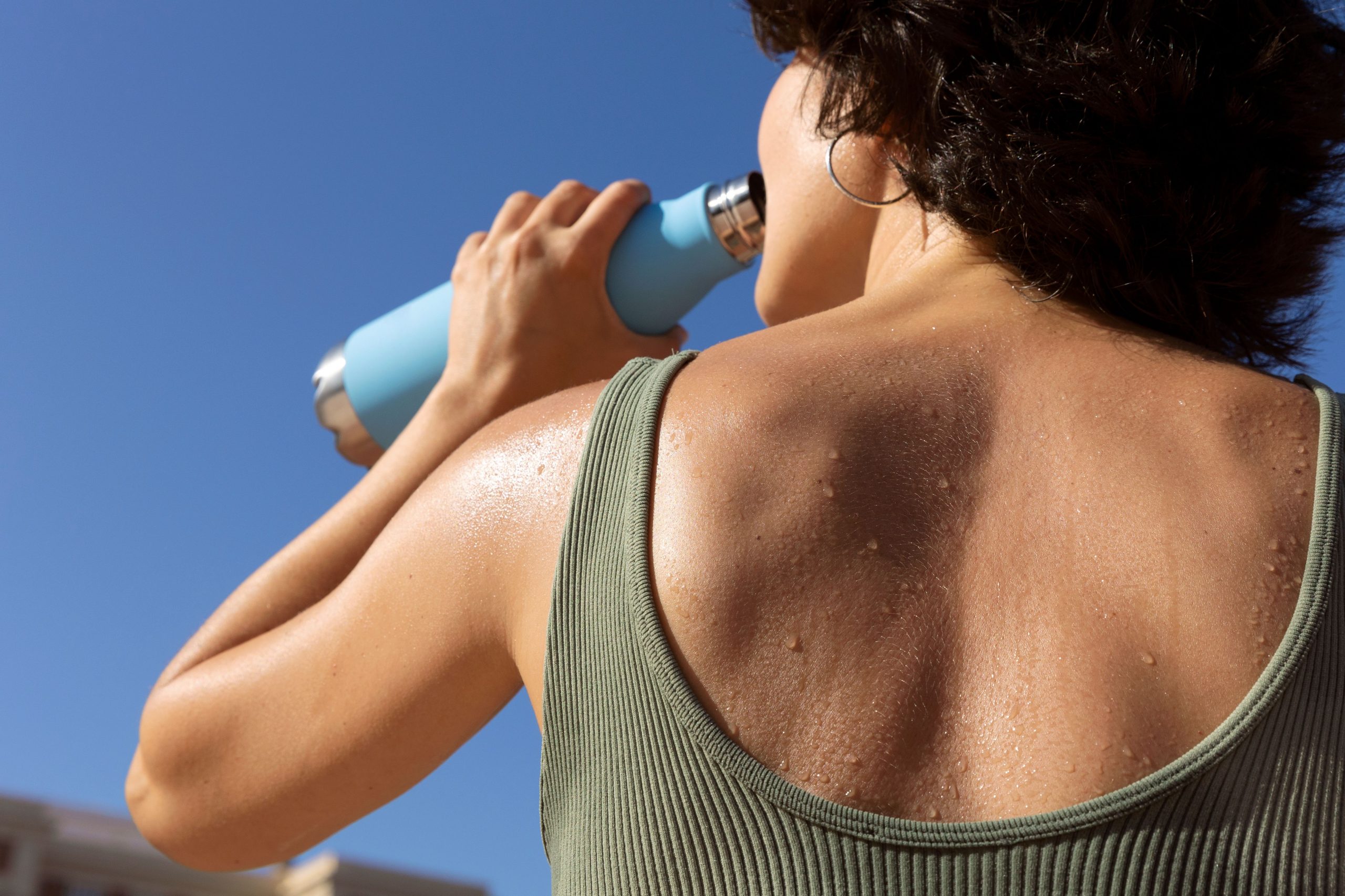 Mulher de costas bebendo água no calor ao ar livre. Foto: FreePik
