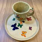 Um pires e uma xícara de cerâmica com borboletas desenhadas.