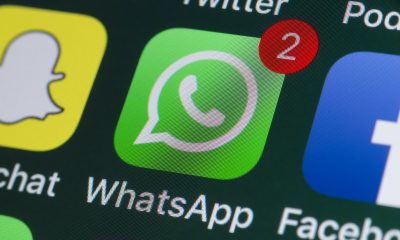 Na imagem aparece a tela de um celular. No centro é o aplicativo do WhatsApp com o característico fundo verde e um balão com um telefone dentro.
