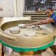 Flávio Fernandes Santos com uma panela de barro gigante de 1,50 metros. Ele mostra com o braço que a panela é grande