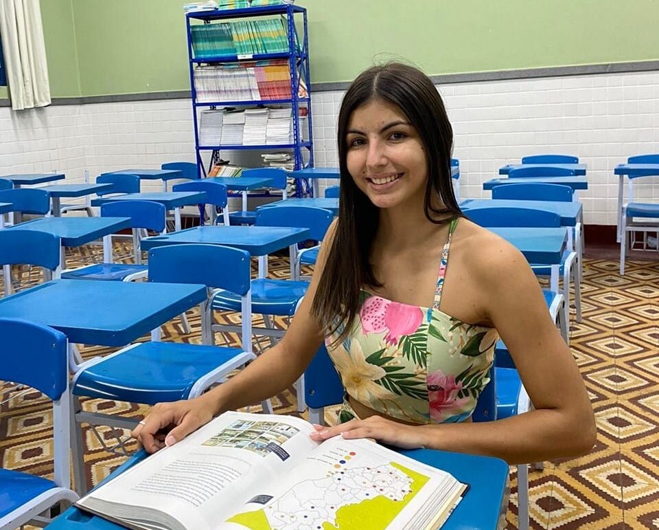 Amanda Teixeira Zampiris tirou nota mil na redação do Enem 2023. Sentada na sala de aula na escola estadual com um livro na carteira.