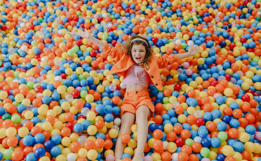 A brinquedolândia, que é uma piscina cheia de bolinhas coloridas e uma criança de roupa laranja se jogando