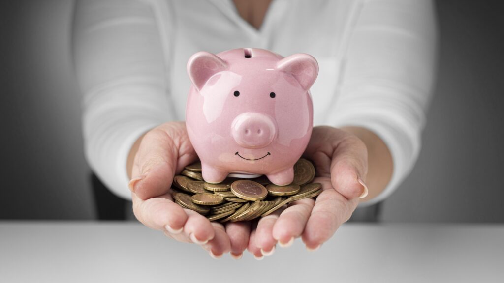 Um cofre em formato de porquinho que representa a poupança nas mãos de uma pessoa com moedas.
