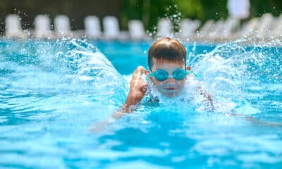 Criança de óculos de natação na piscina aprendendo a nadar.