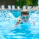 Criança de óculos de natação na piscina aprendendo a nadar.