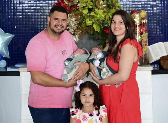 Pai de rosa e a mãe de vermelho com os dois bebês dos sêxtuplos capixabas no colo e a filha mais velha abaixo