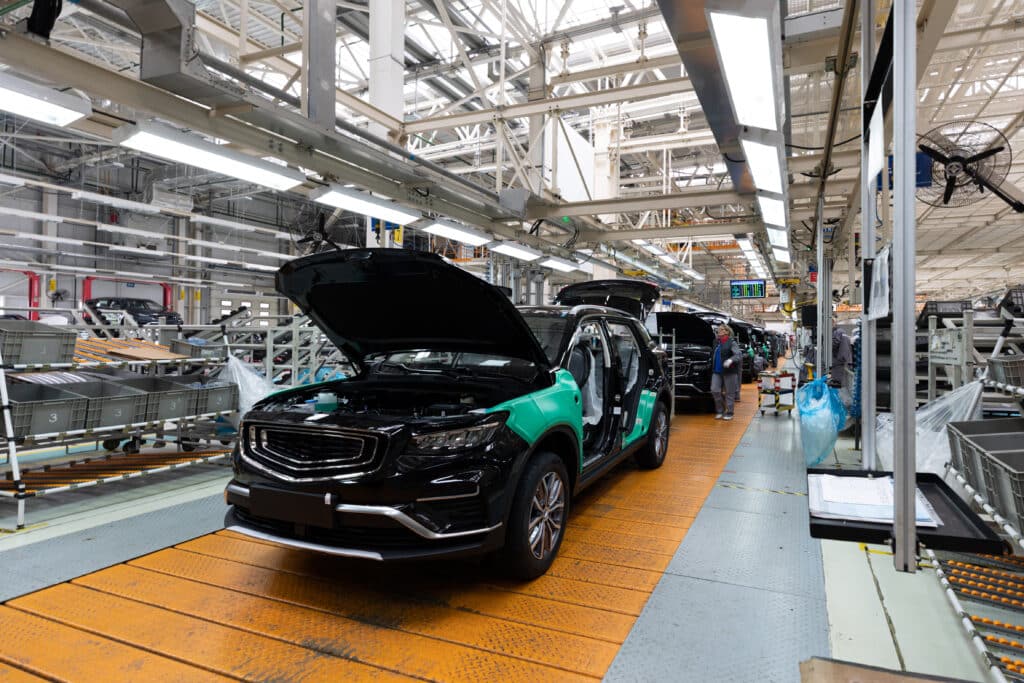 A imagem apresenta um carro sendo fabricado numa indústria automobilística com o capô levantado
