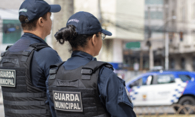 Dois agentes da Guarda Municipal de Vitória uniformizados. Com a viatura ao fundo