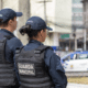 Dois agentes da Guarda Municipal de Vitória uniformizados. Com a viatura ao fundo