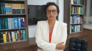 Érica Neves é diretora estadual da Associação Brasileira dos Advogados (ABA) posando pra foto em meio a livros e uma televisão ao fundo