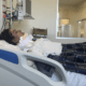 Lindalva Firma deitada em uma cama de hospital na enfermaria. A jovem está paraplégica após lesão durante acidente na Acro-Yoga.