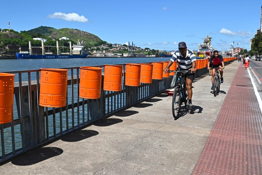 Papeleiras instaladas ao longo da avenida Beira-Mar, no Centro de Vitória para os blocos de rua. Ciclistas passando pela calçada e o mar ao fundo