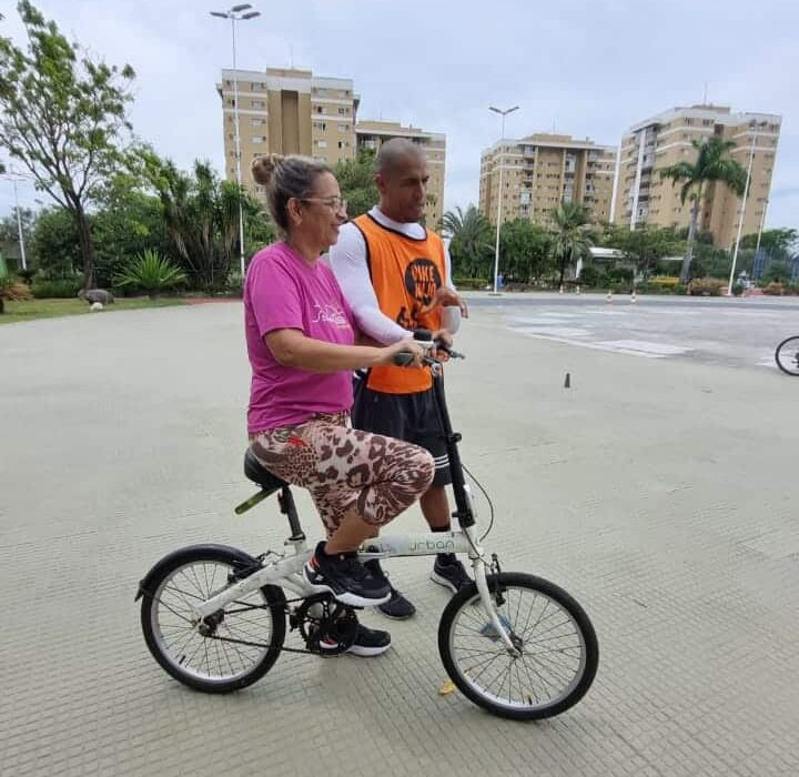 Idosa em cima da bicicleta aprendendo a pedalar com voluntário da Bike Anjo na Praça do Papa, em Vitória