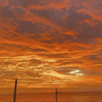 O céu alaranjado no amanhecer e o mar ao fundo da foto