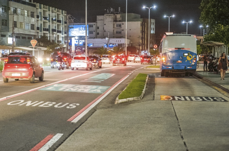 Avenida Dante Michelini, em Vitória, à noite. Da pra ver muitos carros e um ônibus circulando na orla de Camburi