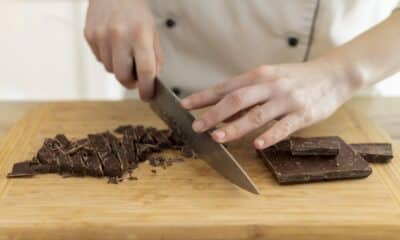 Uma mulher com uma faca cortando uma barra de chocolate em uma tábua