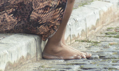 Pés descalços de mulher na rua sentada no meio fio, claramente uma pessoa em situação de rua