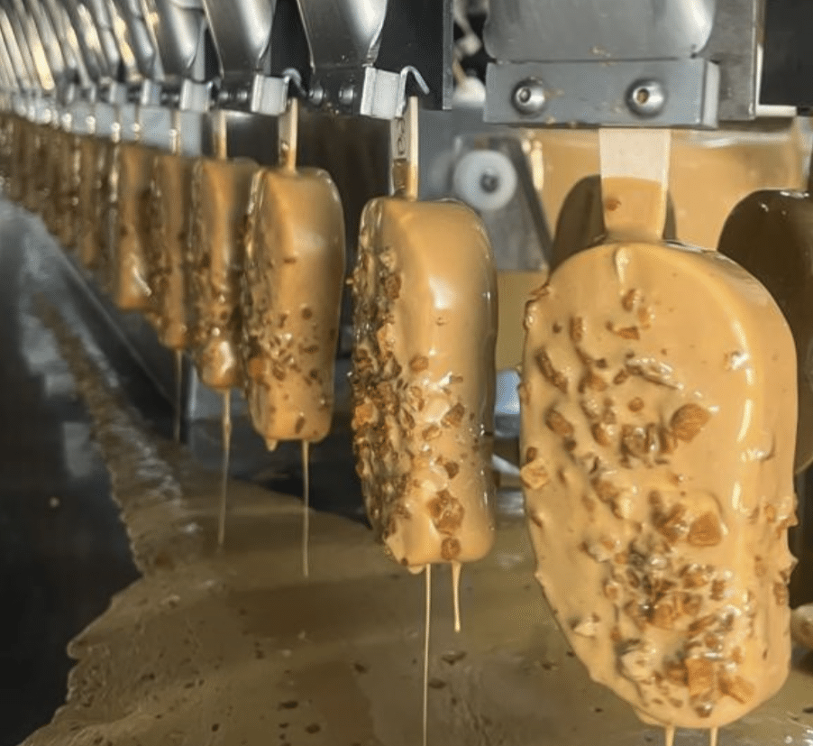Picolés em máquina sendo preparado com cobertura do Grupo Lamoia, fabricante de sorvete