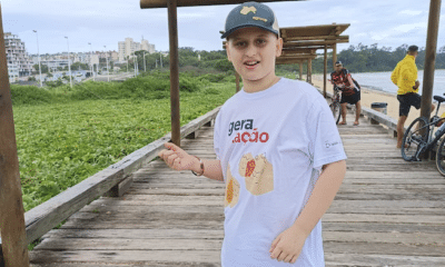 Victor Bonomo Trés, 12 anos, de boné, camisa e bermuda. Ele posa em uma estrutura de madeira próximo à praia