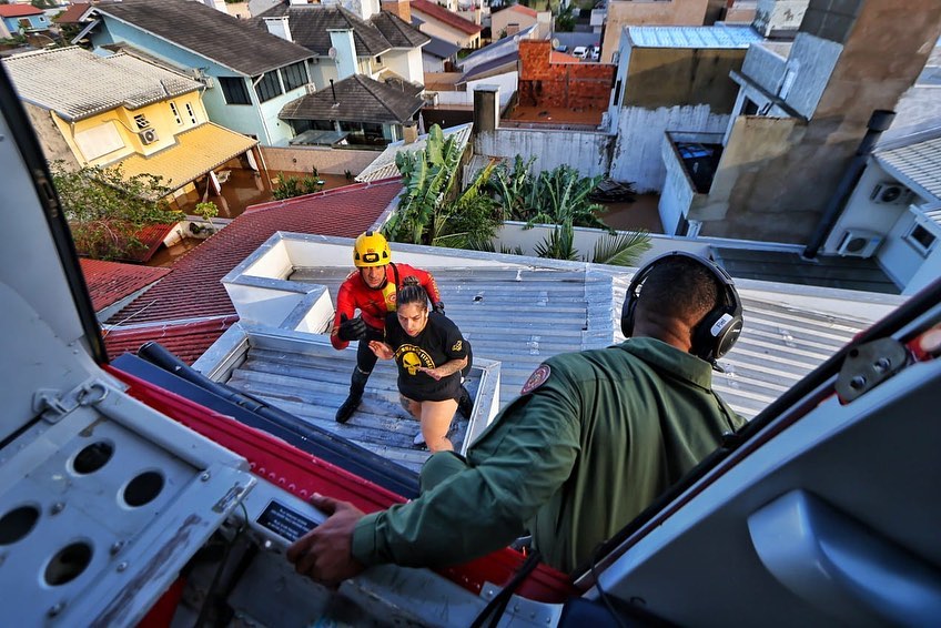 Bombeiro olhando do helicóptero mulher ser resgatada do teto de casa em cidade alagada após chuvas fortes no Rio Grande do Sul