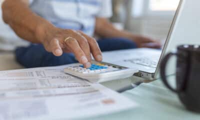 Um homem fazendo conta em uma calculadora com diversos papéis e um computador