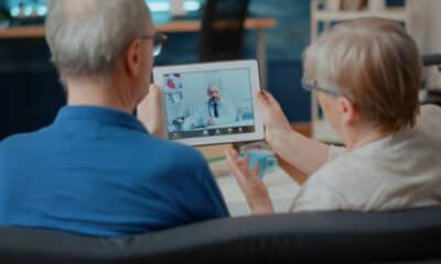 Um casal de idosos sentados com um tablete na mão passando por uma consulta de telemedicina