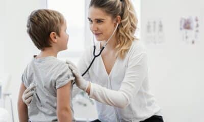 Uma criança na frente de uma médica cardiologista que está com o estetoscópio auscultando o coração
