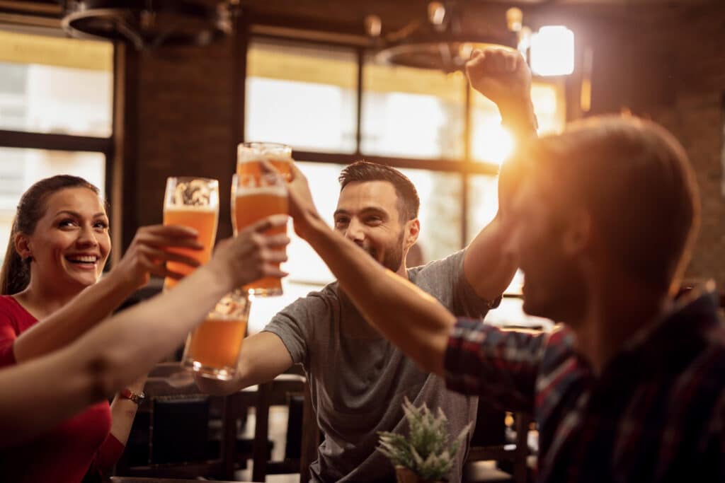 Pessoas reunidas ao redor de uma mesa brindando com copos de cerveja