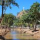 Um rio com árvores e ao fundo o Cristo Redentor de Mimoso do Sul