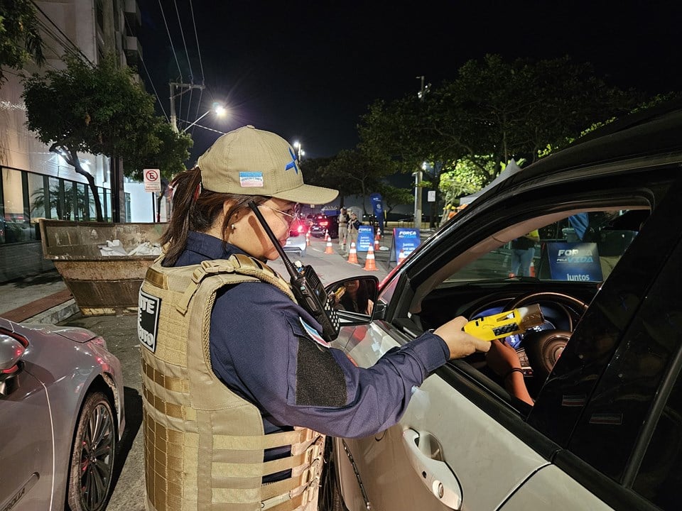 Uma agente de trânsito com bafômetro na mão na janela de um carro de um motorista