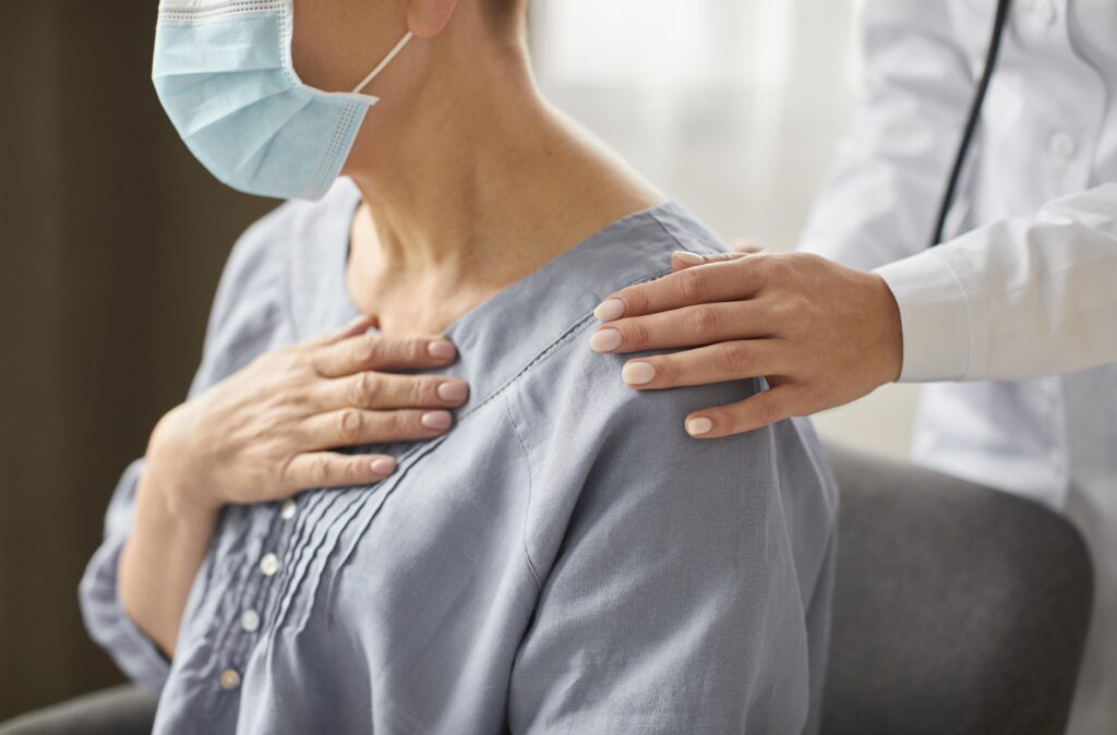 Uma paciente com câncer com um médico atrás apoiando nos ombros
