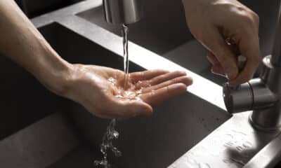 Água saindo da torneira e caindo na mão de uma mulher que abre a torneira