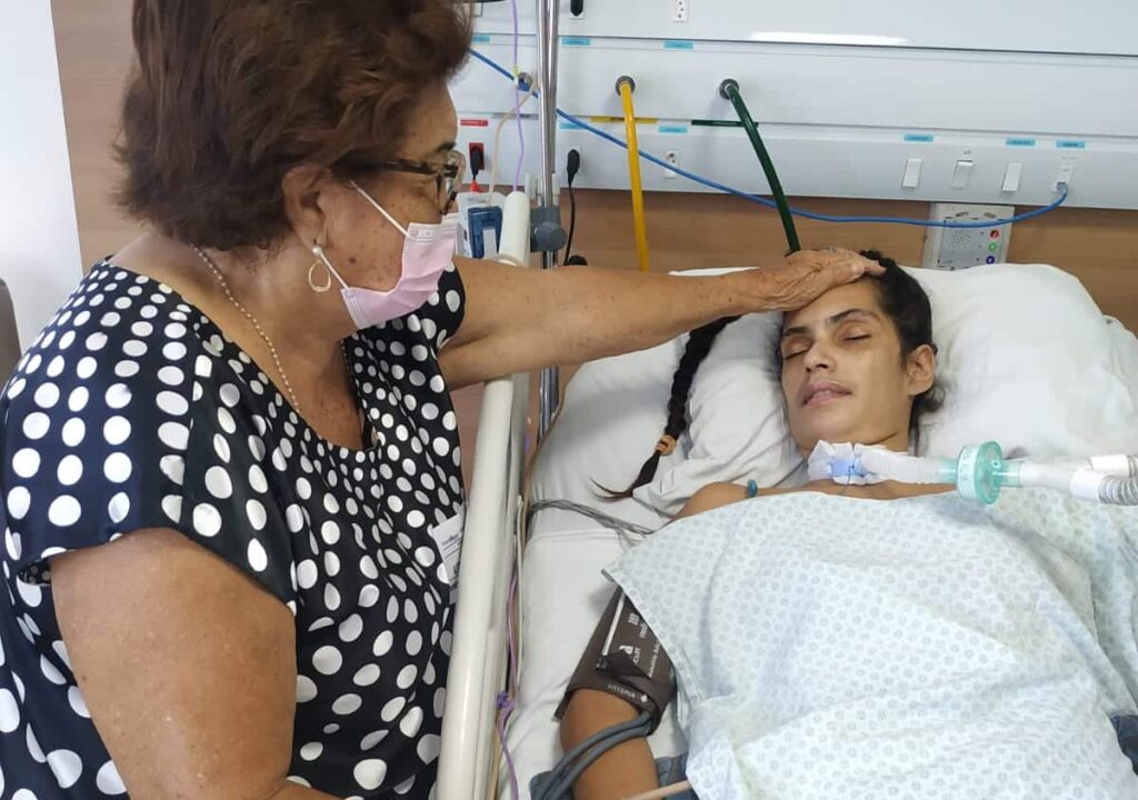 Desirée no leito hospitalar recebendo cuidados da avó durante a internação após diagnóstico de botulismo