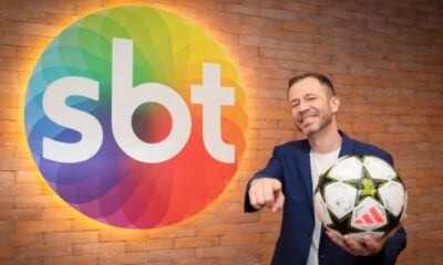 Thiago Leifert na frente da logo do SBT com uma bola de futebol na mão