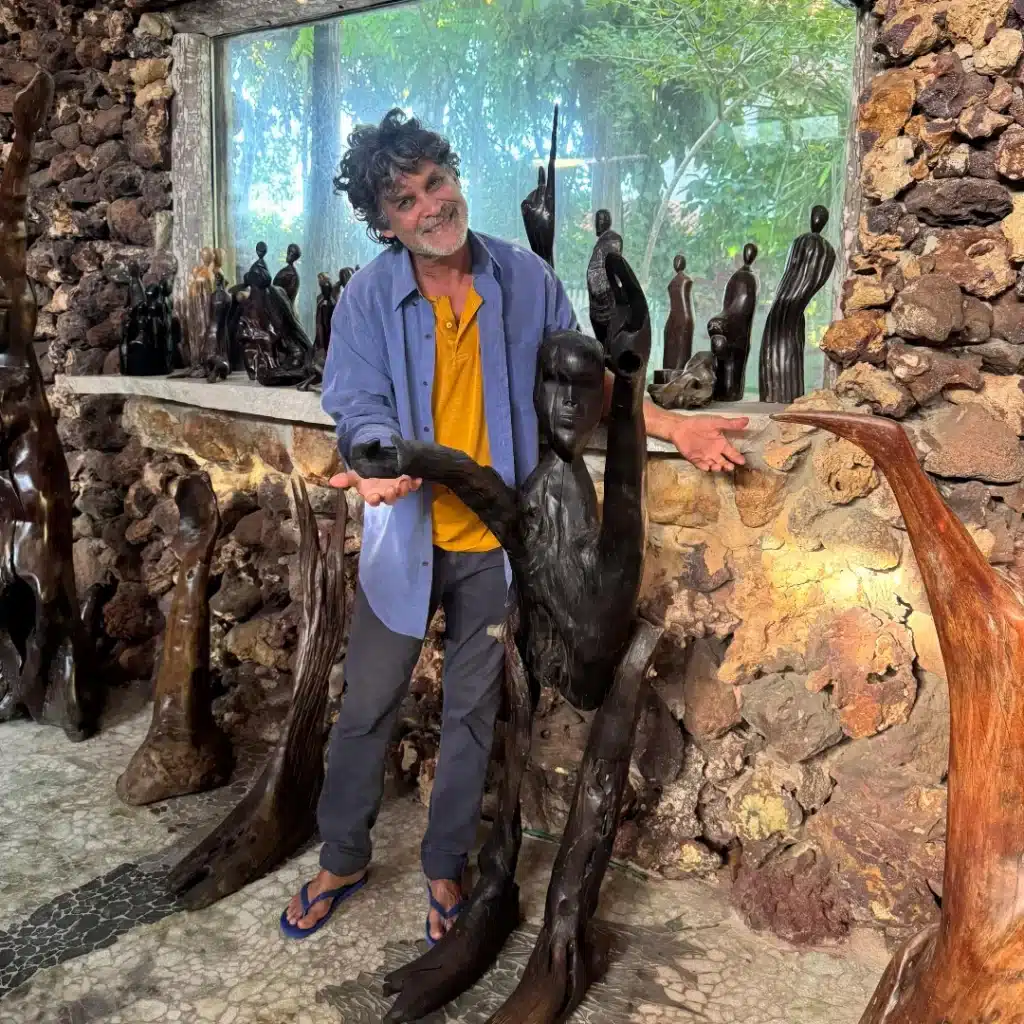 O artista Neusso Ribeiro posa com uma de suas esculturas em madeira, na Casa de Pedra