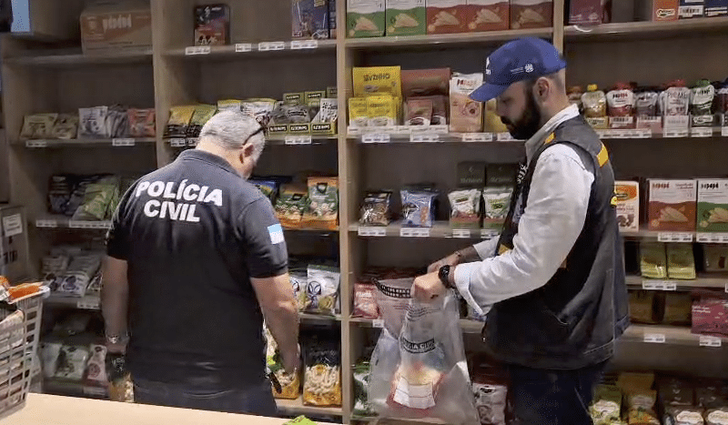 Agentes da Polícia Civil e do Procon-ES recolhem pacotes de biscoitos com rótulo irregular em loja de produtos naturais na Grande Vitória